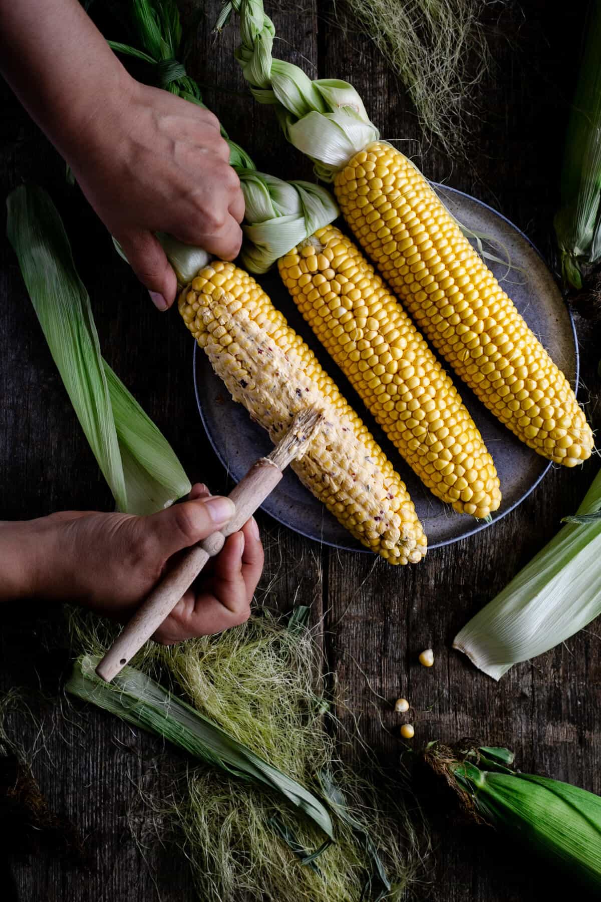 Spreading chilli-infused butter on cobs of corn with pastry brush