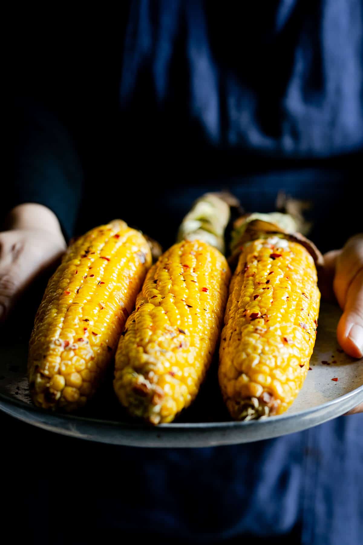 A person holding a plate with cobs of corn in chilli butter