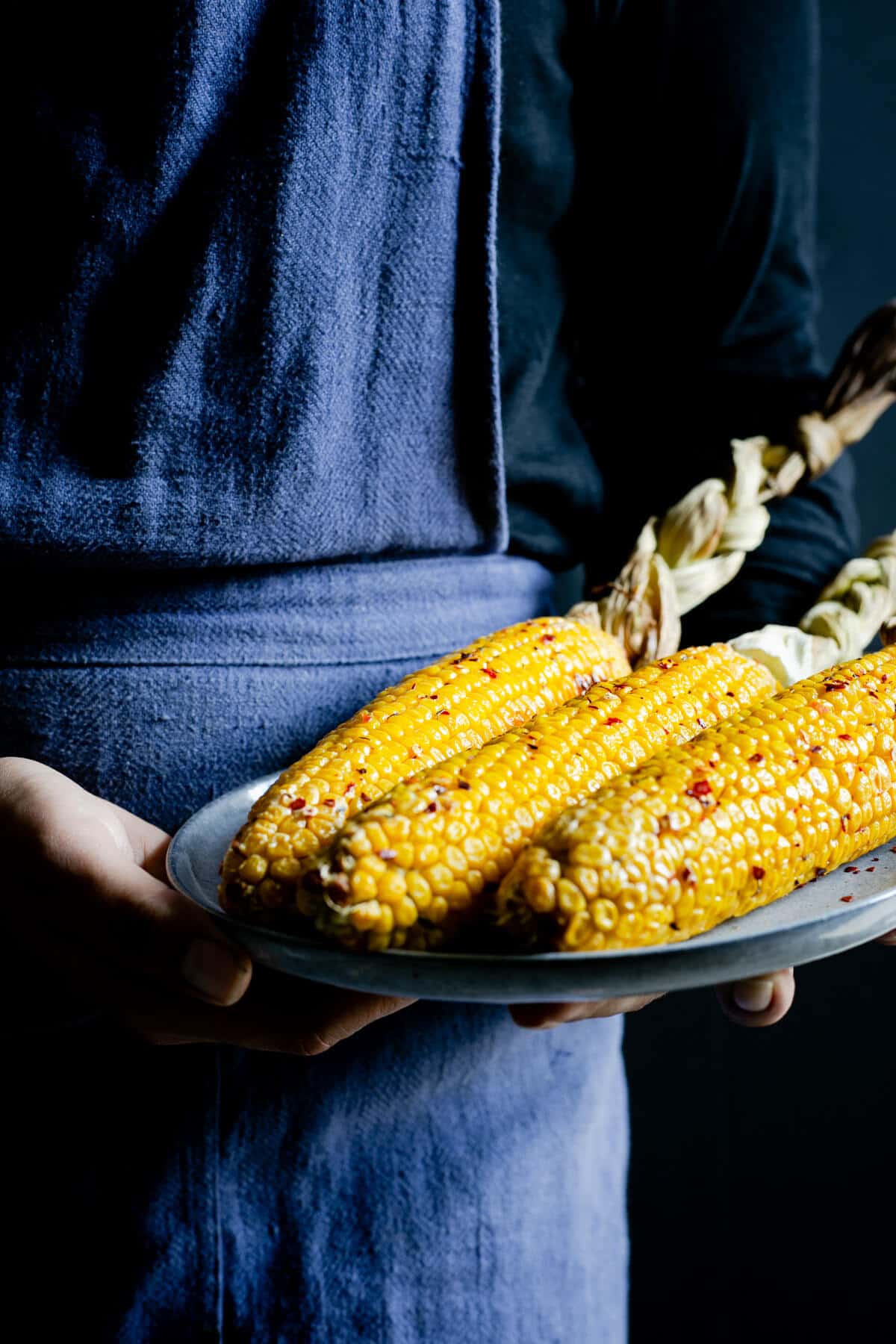 A person holding a plate with buttered corn on the cob