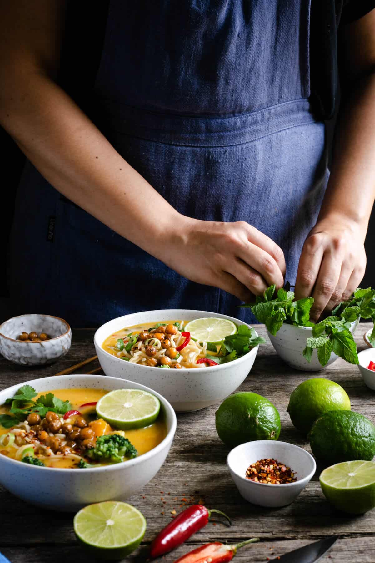 A person topping up two bowls of Thai style pumpkin laksa with fresh mint