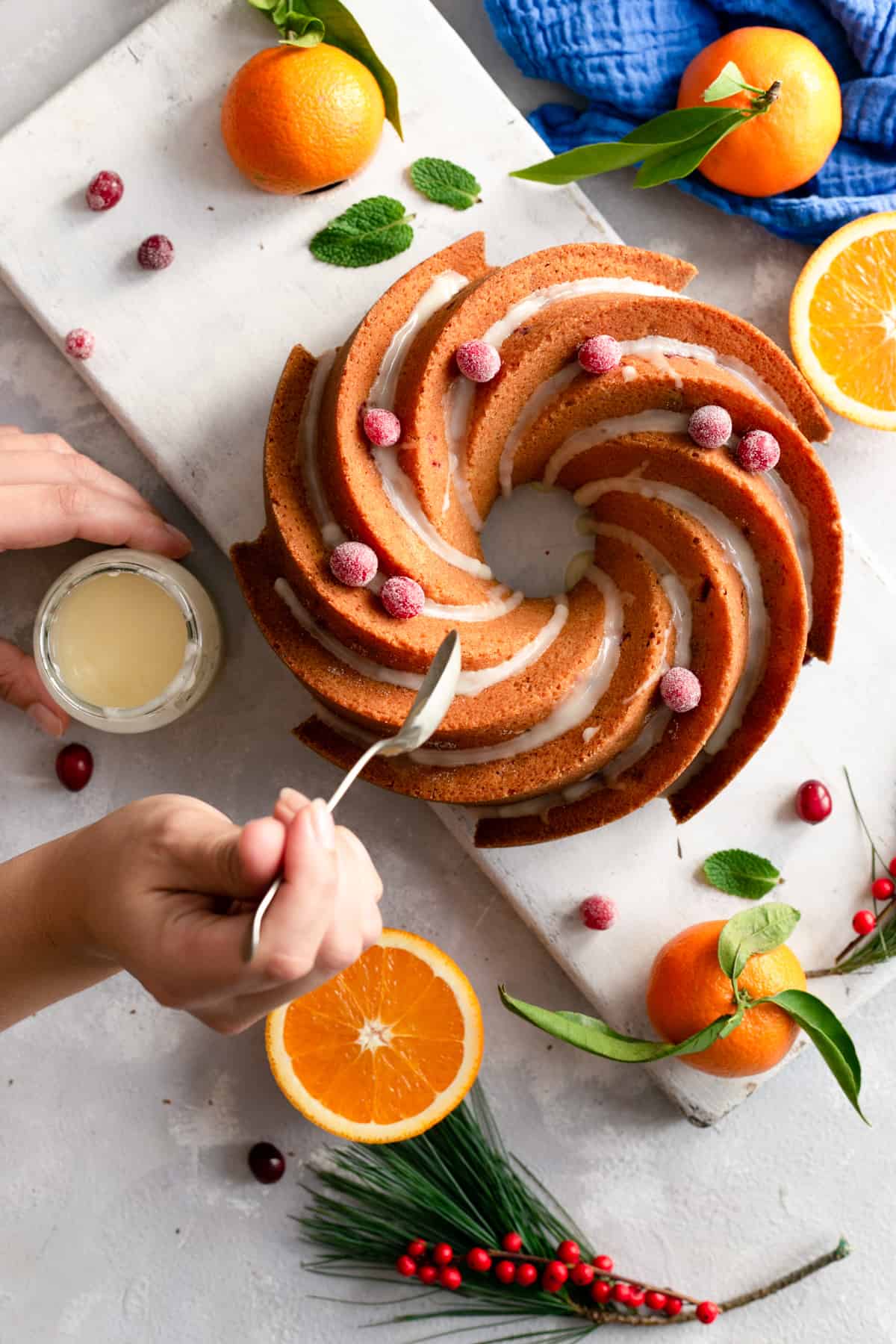 Overhead shot of a person drizzling orange and cranberry bundt cake with some icing