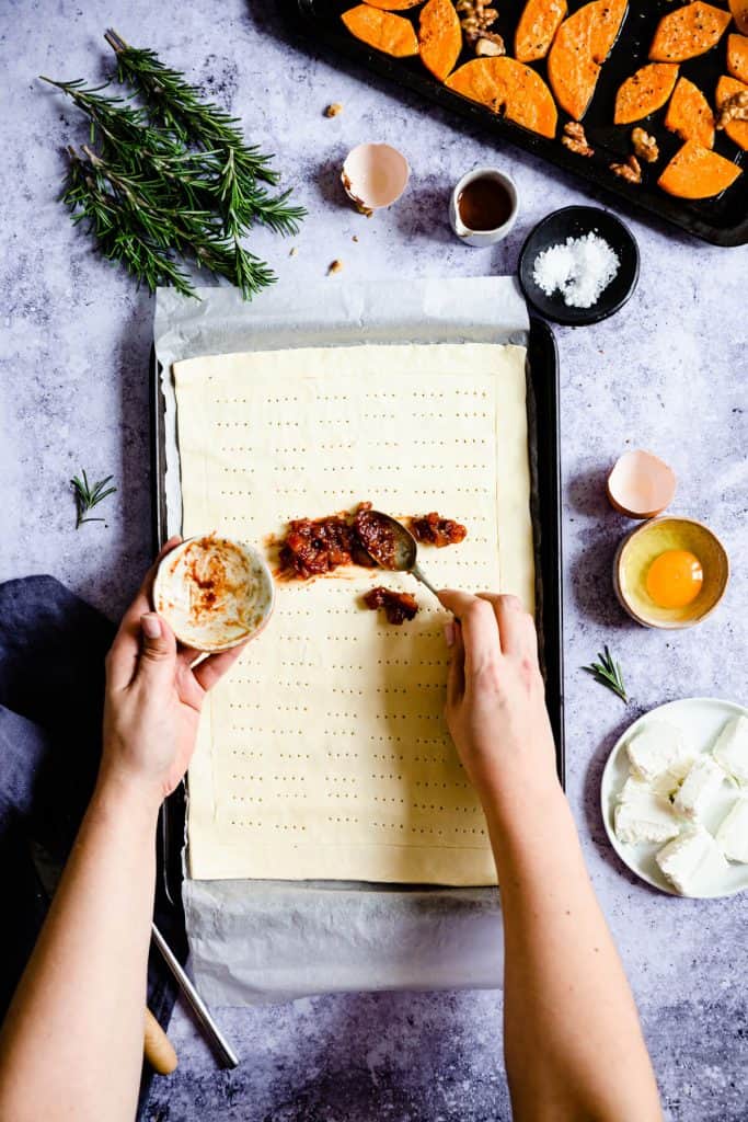 overhead shot of a person spreading chutney on puff pastry