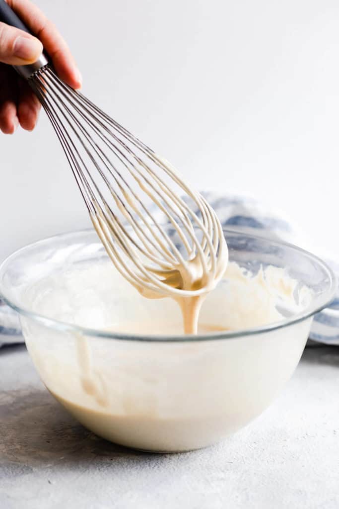 side close up of a pancake batter dripping from a whisk