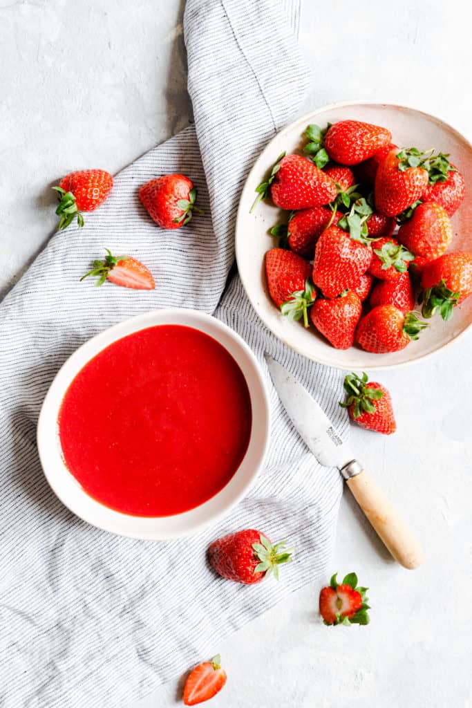 top view of a bowl of strawberry puree and fresh strawberries
