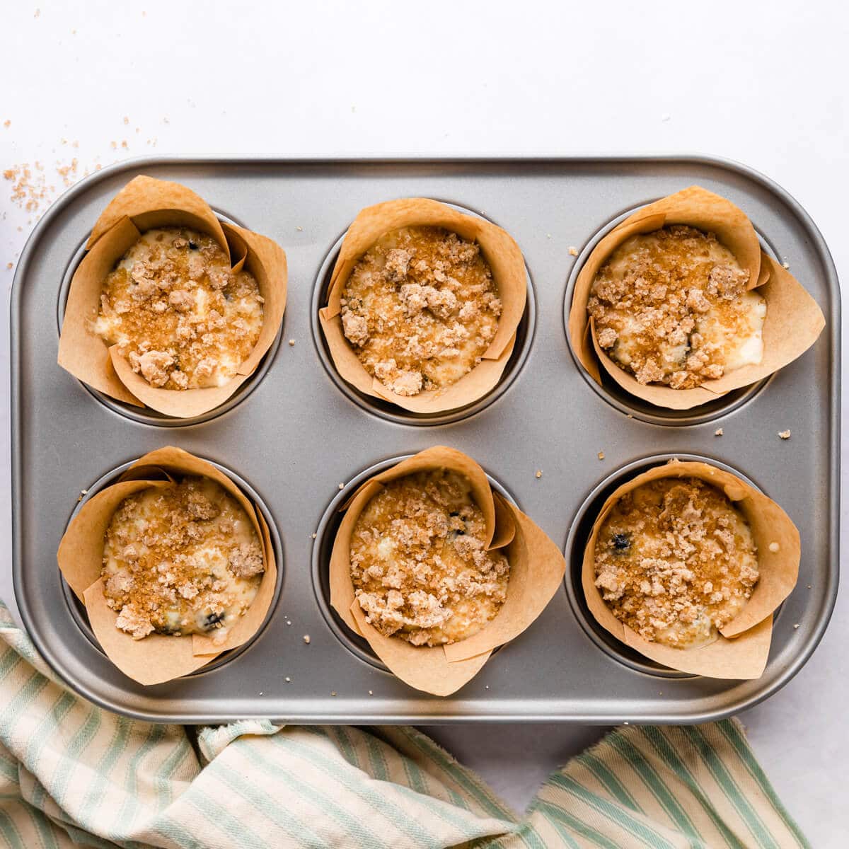 muffin batter topped with streusel inside of the muffin cases in the baking tin.
