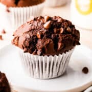chocolate muffin in a paper case on a small white plate.