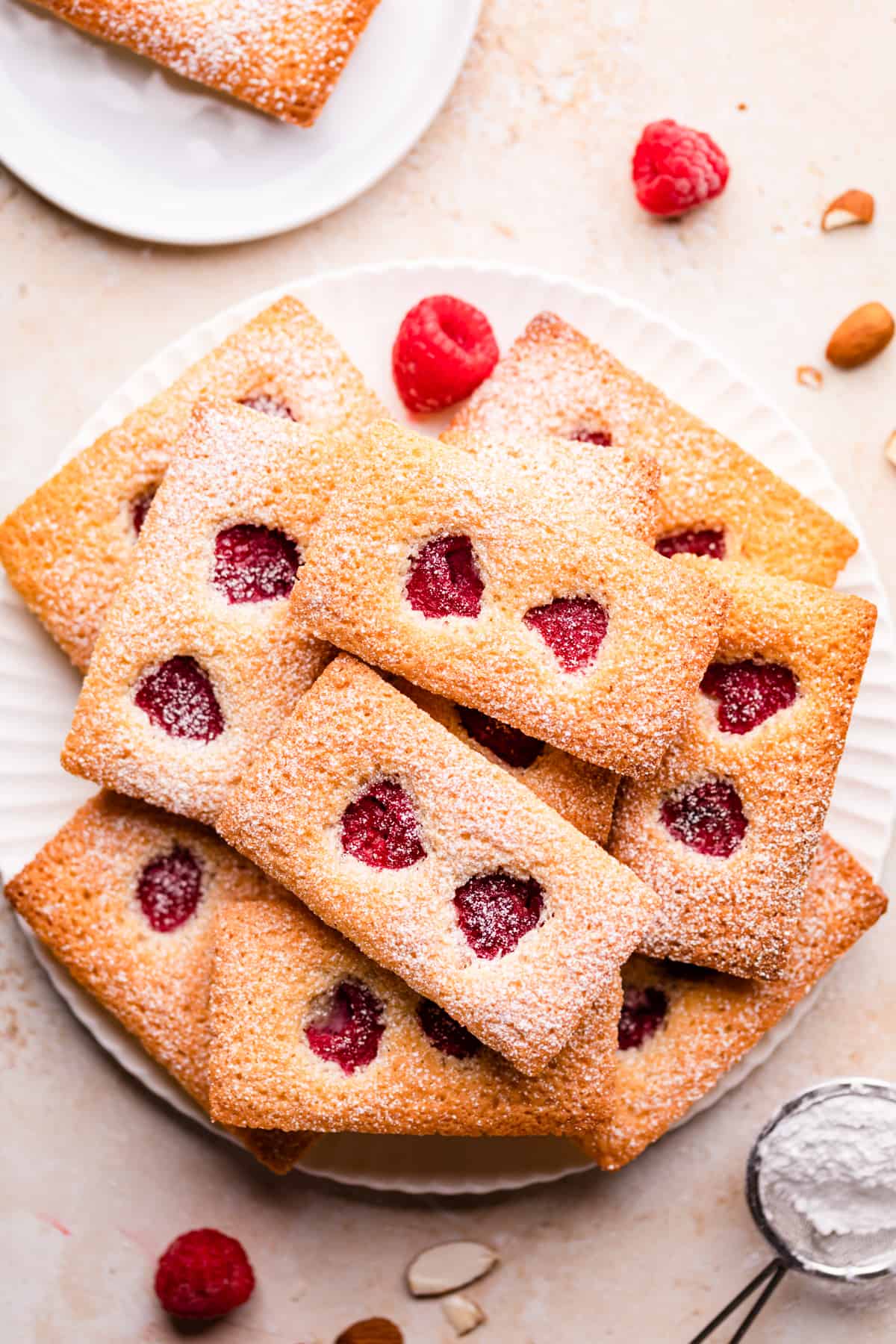 small rectangular financier cakes with raspberries and icing sugar on a white plate.