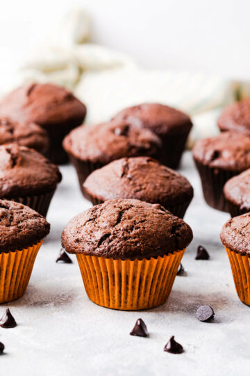 plain chocolate muffins in orange and brown cases with some chocolate chips around them.