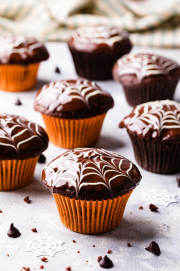 chocolate fudge spiderweb muffins in orange muffin cases standing on a light surface.