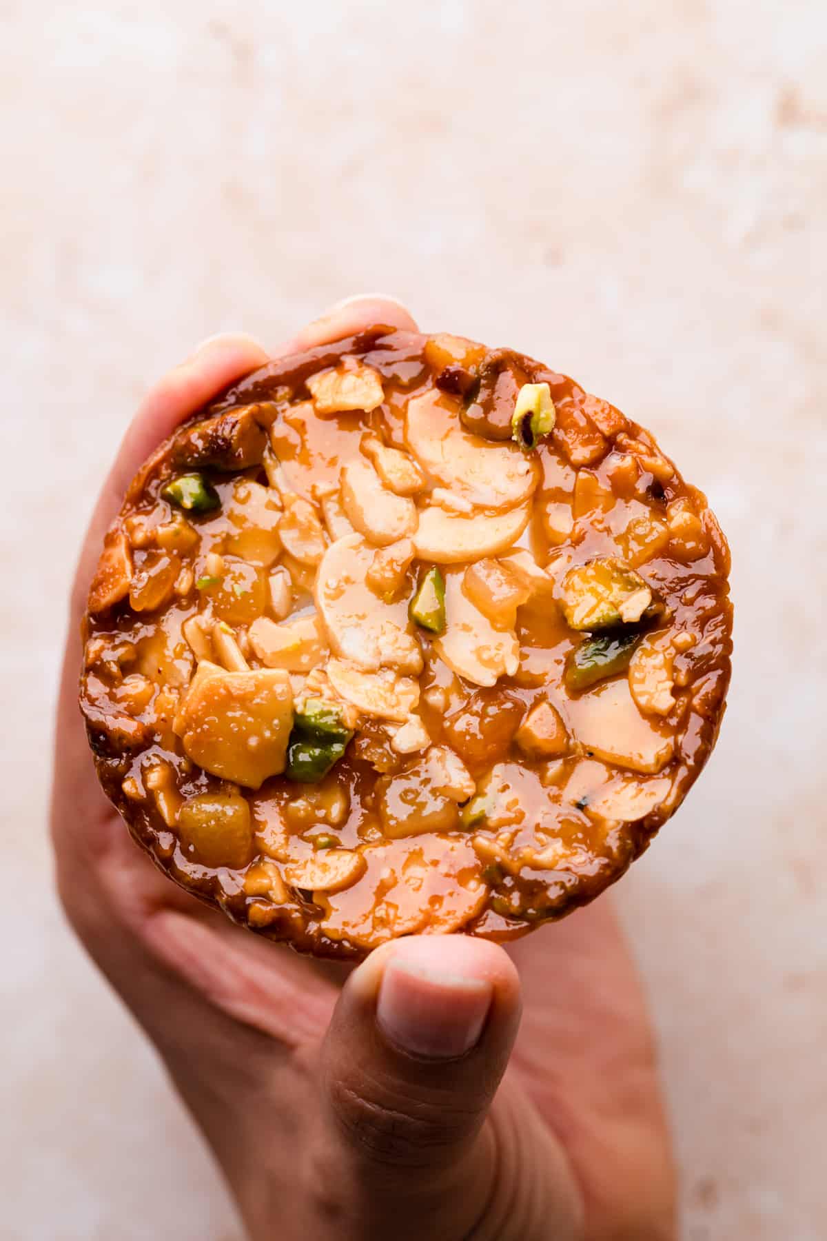 individual almond florentine cookie with pistachio nuts and fruit peel being held by hand.