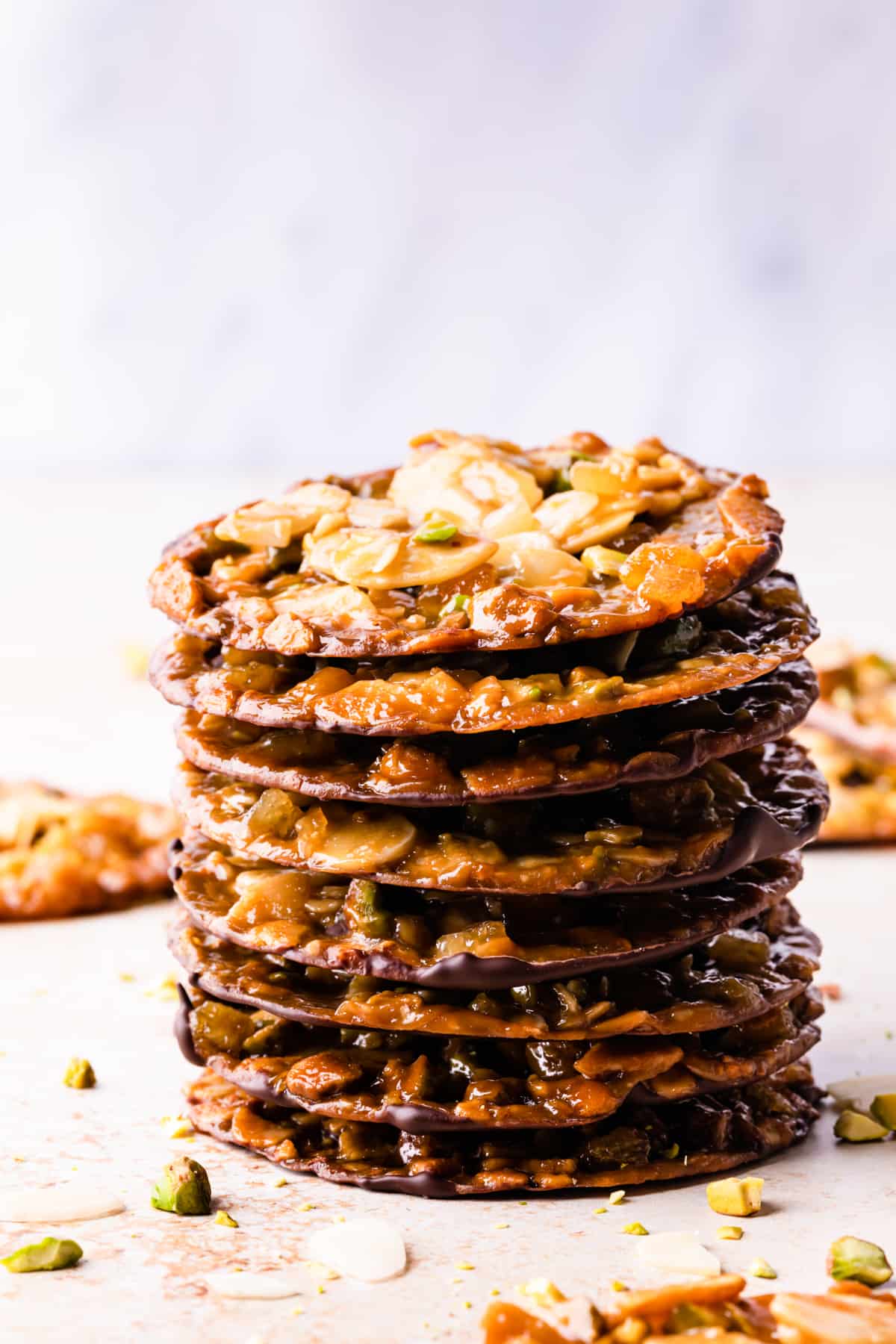 stack of vegan florentines with almonds and pistachios and some chopped nuts around them.