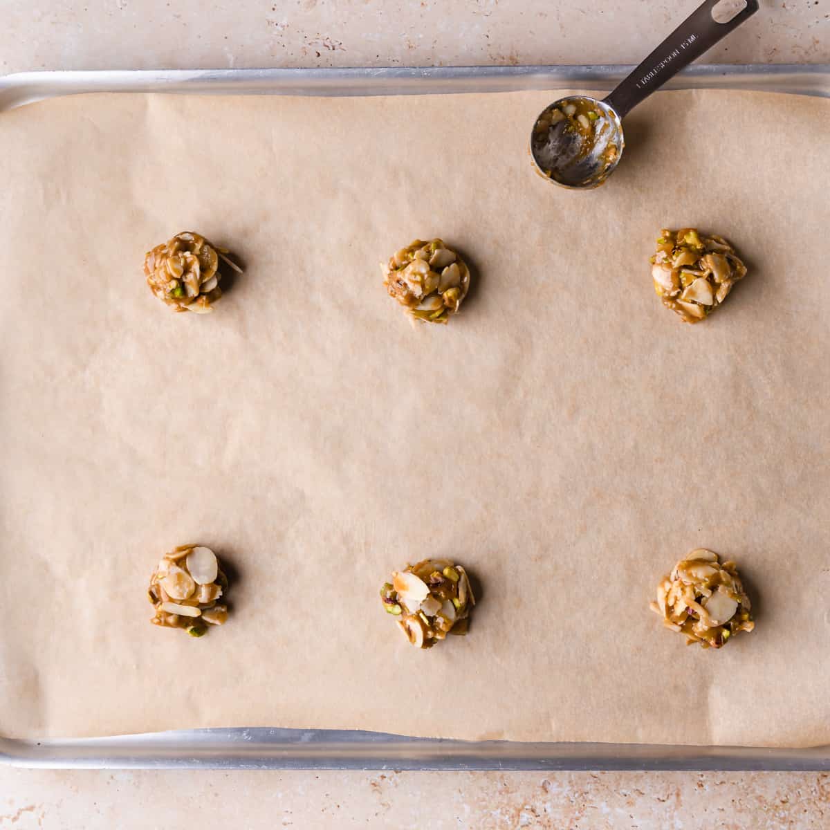 baking sheet lined with baking parchment and small balls of almond florentines mixture and measuring spoon on the baking tray.