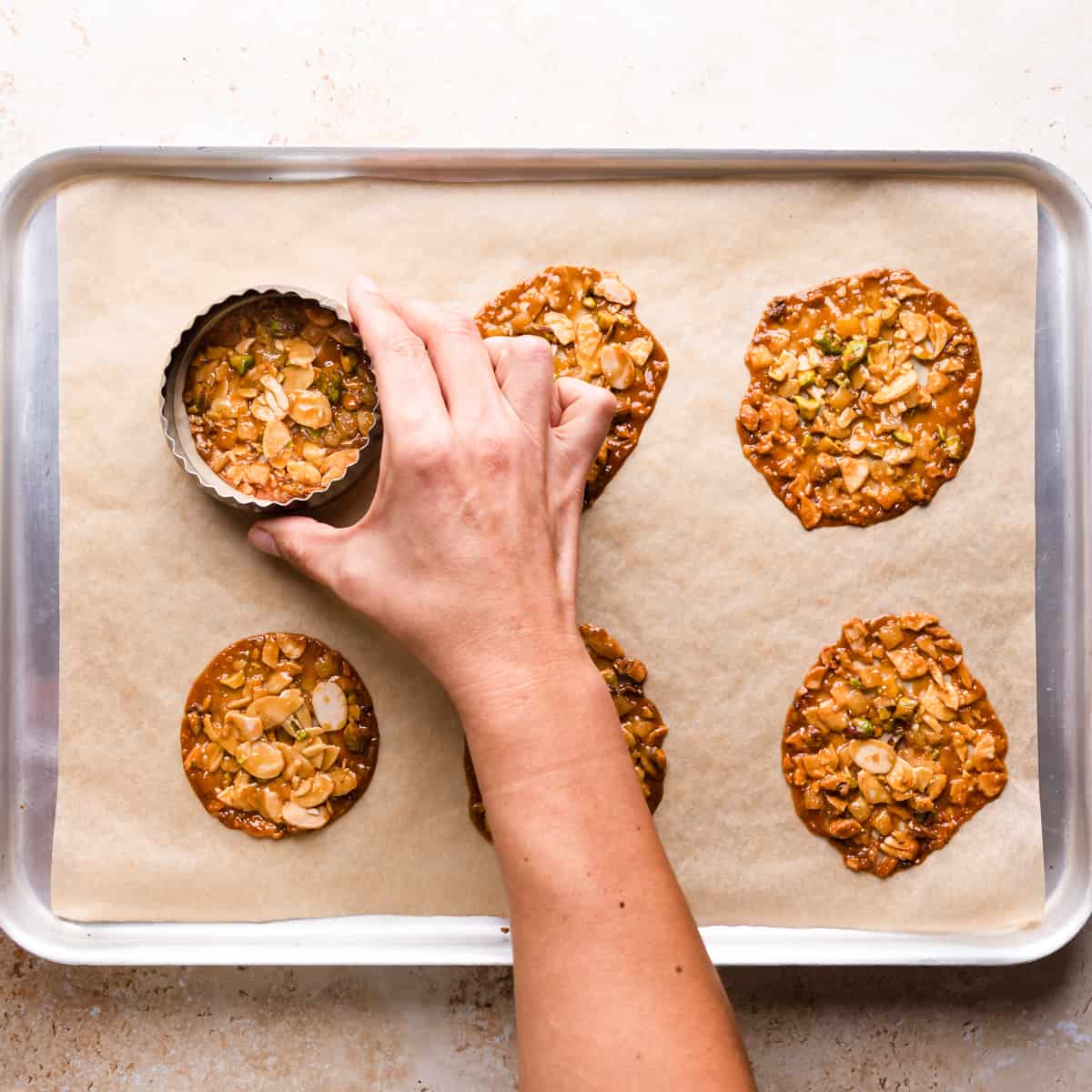 baked florentines with almonds and pistachios being pressed into rounds with cookie cutter.