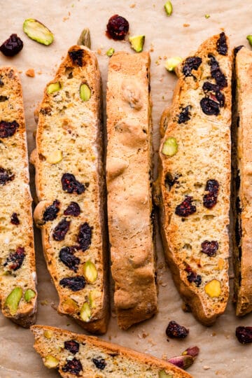 crispy cranberry biscotti slices with crushed pistachios and dried cranberries scattered around them.