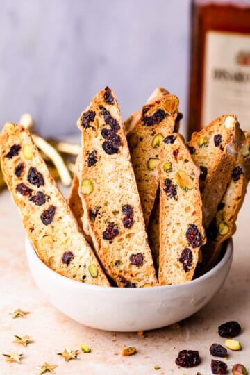 biscotti cookies standing up inside of ceramic bowl with some dried cranberries on side.