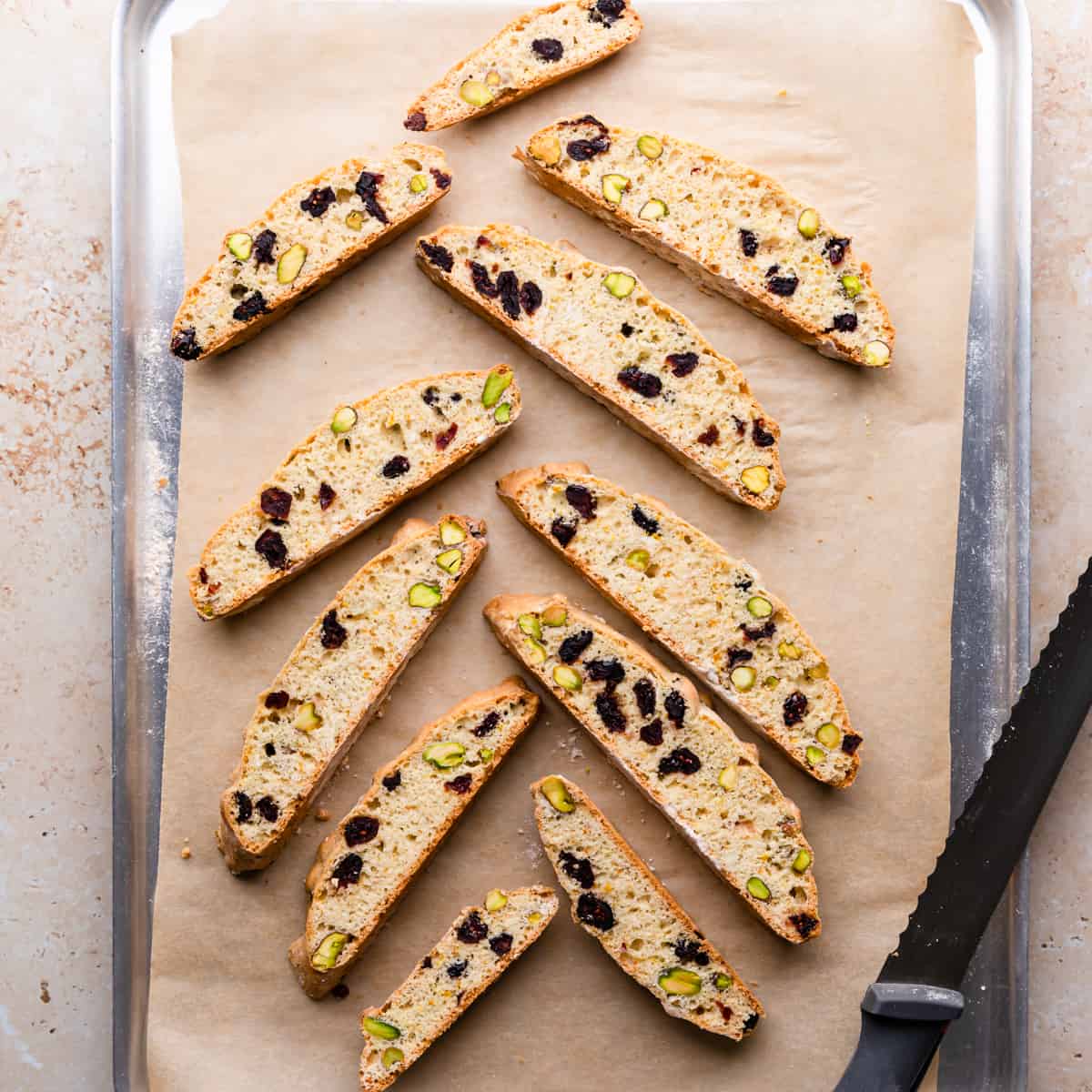 cranberry biscotti baked once on top of baking tray with serrated knife on side.