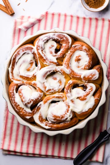 round baking dish with vegan sweet potato cinnamon buns and frosting spread on top of them.