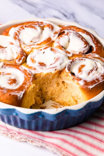 blue round pie dish with fluffy vegan sweet potato cinnamon rolls topped with frosting.