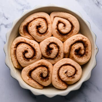 doubled in size slices of vegan sweet potato cinnamon rolls before baking inside of the round pie dish.