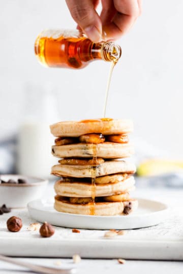 side close up at a stack of pancakes and some maple syrup being poured over them