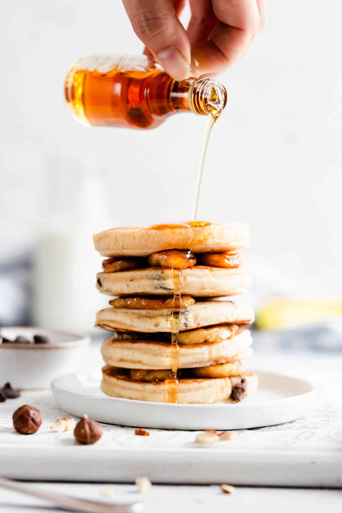 side shot of stack of pancakes and maple syrup being drizzled on them