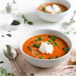 Two bowls of roasted tomato soup topped with sesame and pumpkin seeds