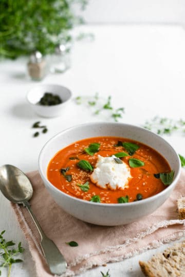 Small bowl of roasted tomato soup topped with fresh basil and ricotta cheese