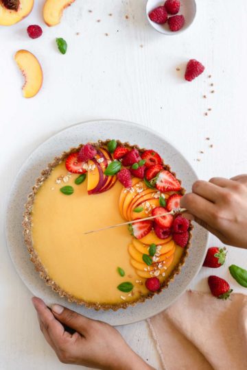 Cutting a slice of vegan peach tart topped with fresh summer berries