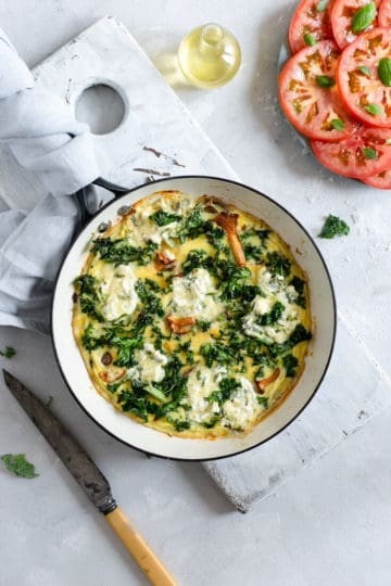Mushroom and kale frittata in the pan with fresh tomato and basil salad