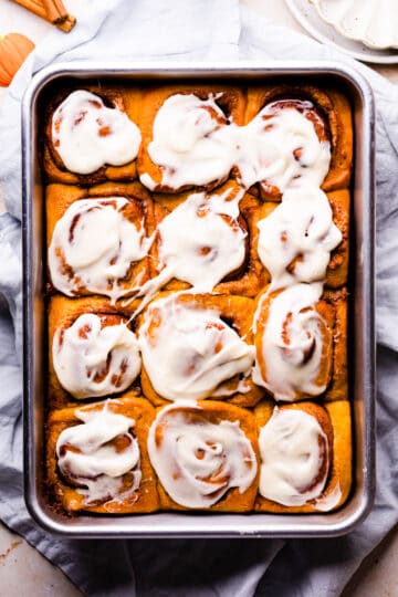 pumpkin buns with cream cheese glaze on top arranged in a baking dish.