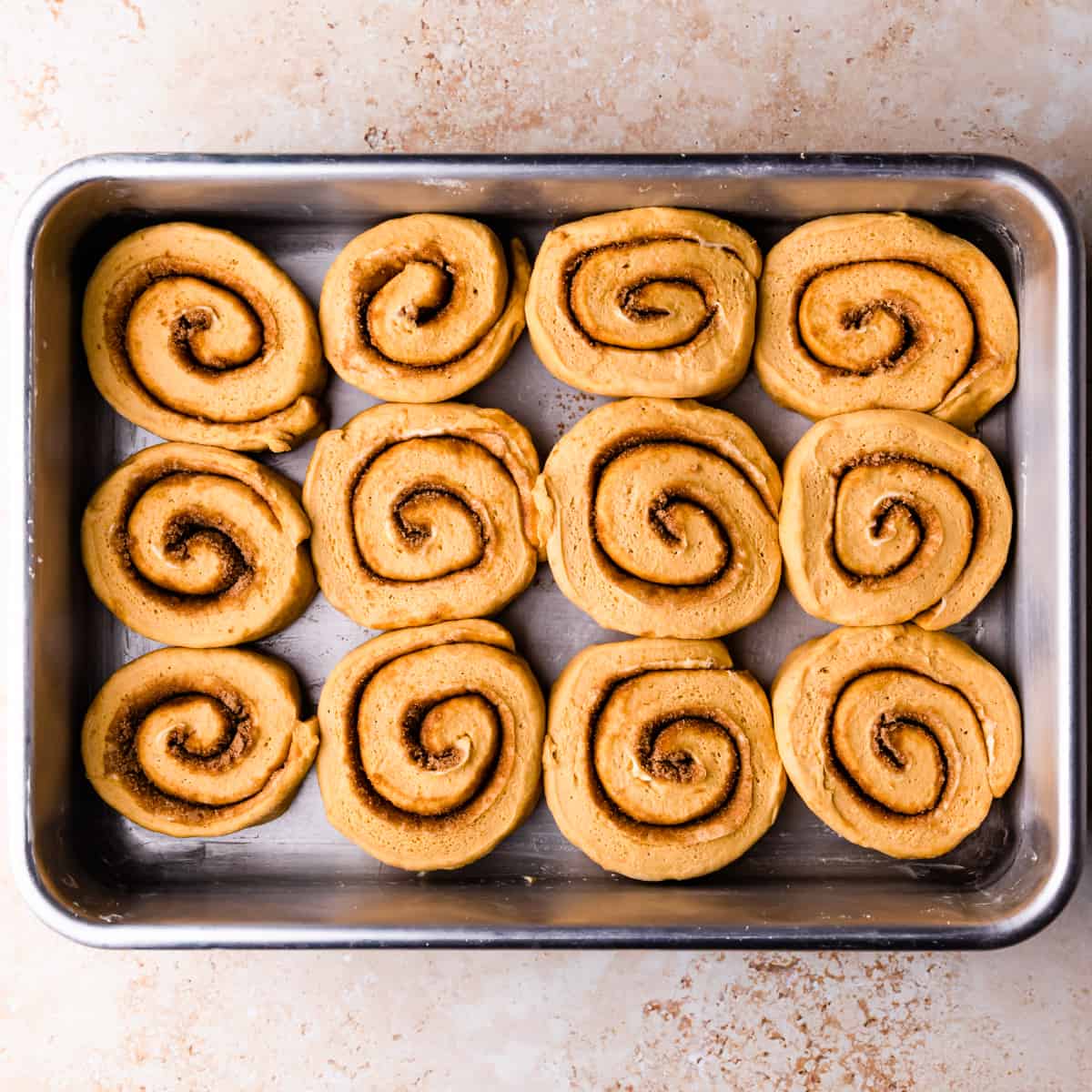 pumpkin cinnamon rolls arranged in a baking dish for second rise.