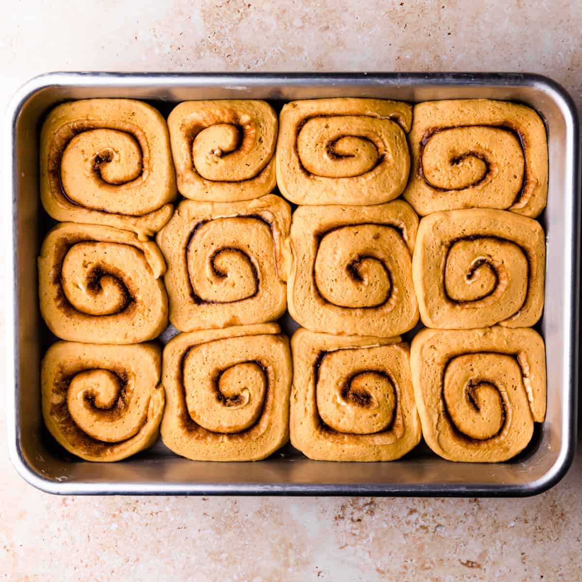 risen cinnamon pumpkin rolls in a rectangular baking dish.