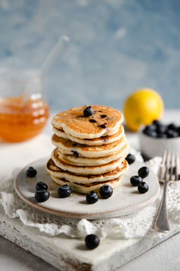 Straight ahead shot of blueberry pancakes on a small plate with honey jar at the back