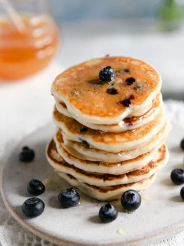 Stack of blueberry pancakes drizzled with honey on a small plate