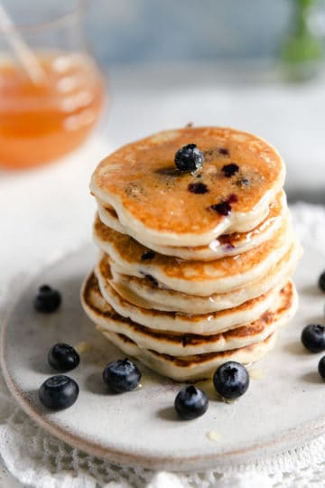 Stack of blueberry pancakes drizzled with honey on a small plate