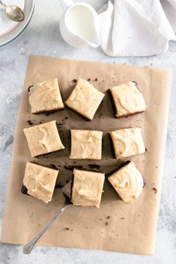 Overhead shot of chocolate brownies with peanut butter frosting on brown baking parchment