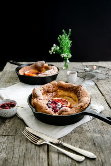 Two small skillets with mixed berry Dutch babies on a wooden table with