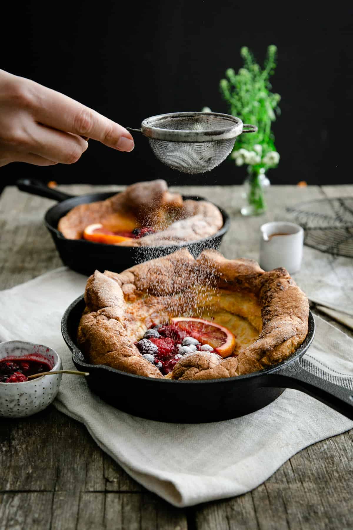 Icing sugar being sprinkled on Dutch baby pancake with mixed berries