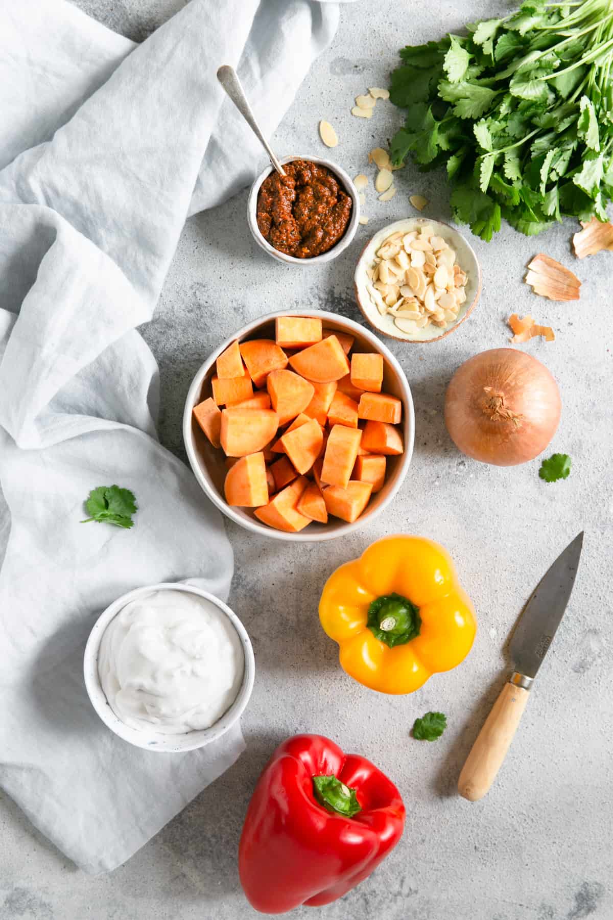 overhead shot of the ingredients for sweet potato curry; peppers, coconut milk, sweet potato, onion, toasted almonds, coriander, curry paste