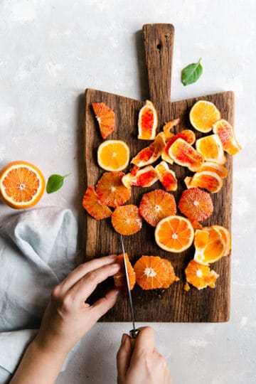 overhead shot of a person slicing a blood orange on a wooden chopping board