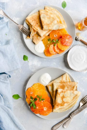 overhead shot of two plates with crepes, citrus, yogurt and honey drizzle