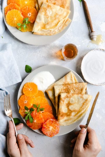 overhead shot of a plate with crepes, citrus slices and yogurt with honey