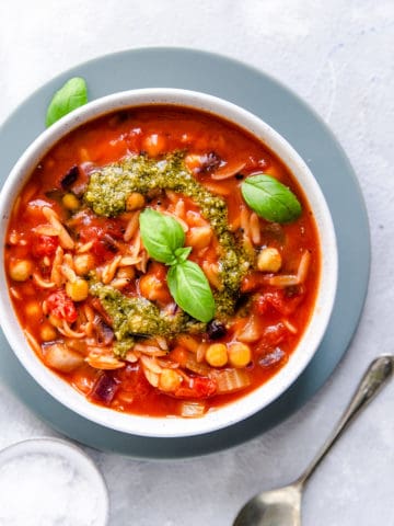 close-up of orzo and tomato soup topped with pesto and fresh basil