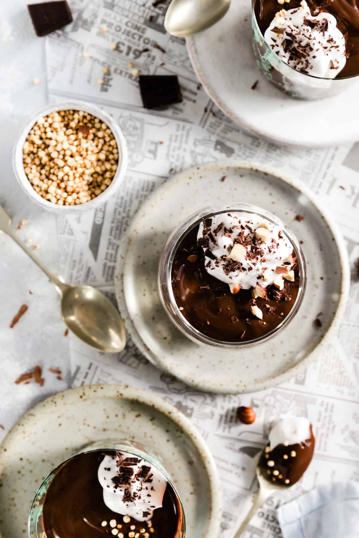 overhead shot of glass filled with vegan chocolate pudding topped with whipped coconut cream, puffed quinoa, hazelnuts and chocolate shavings