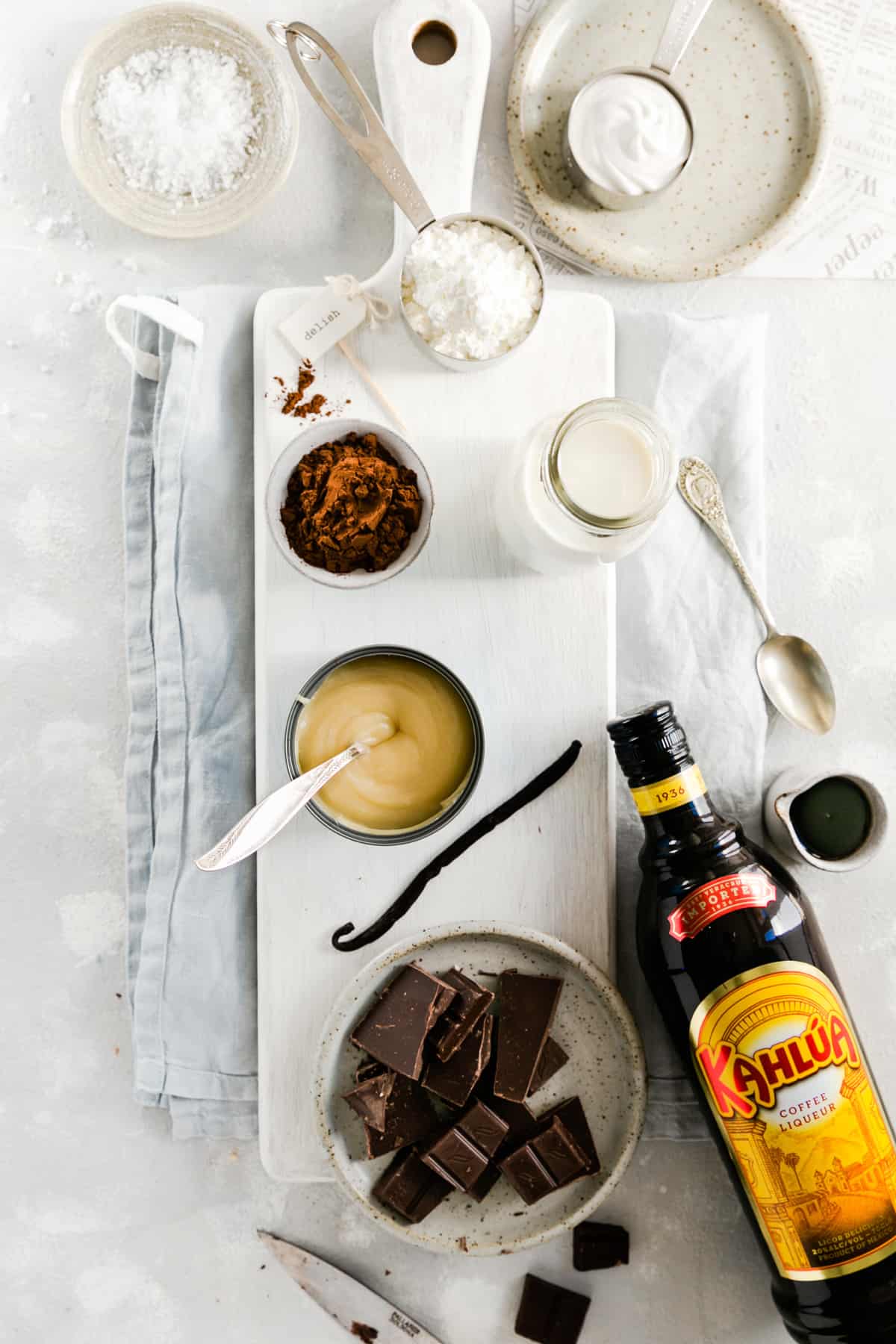 Overhead shot of the ingredients for the vegan chocolate pudding: dark chocolate, coffee liquor, condensed coconut milk, almond milk, cocoa, cornflour, salt and vanilla