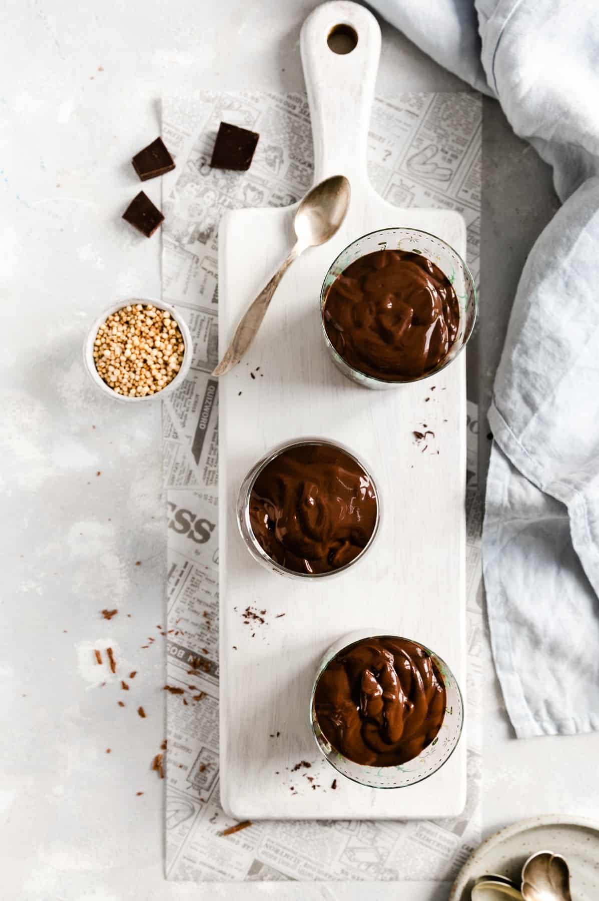 overhead shot of 3 glasses with vegan chocolate pudding on a small white chopping board