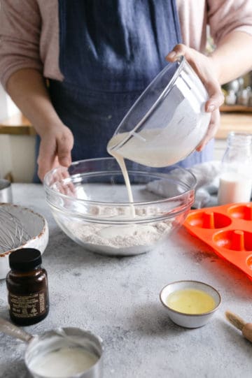 a person pouring wet ingredients mixture into a large bowl with dry ingredients