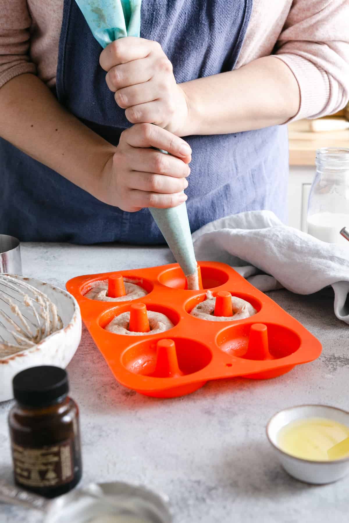 a person holding a piping bag with batter for baked doughnuts, filling the silicone doughnuts mould with batter