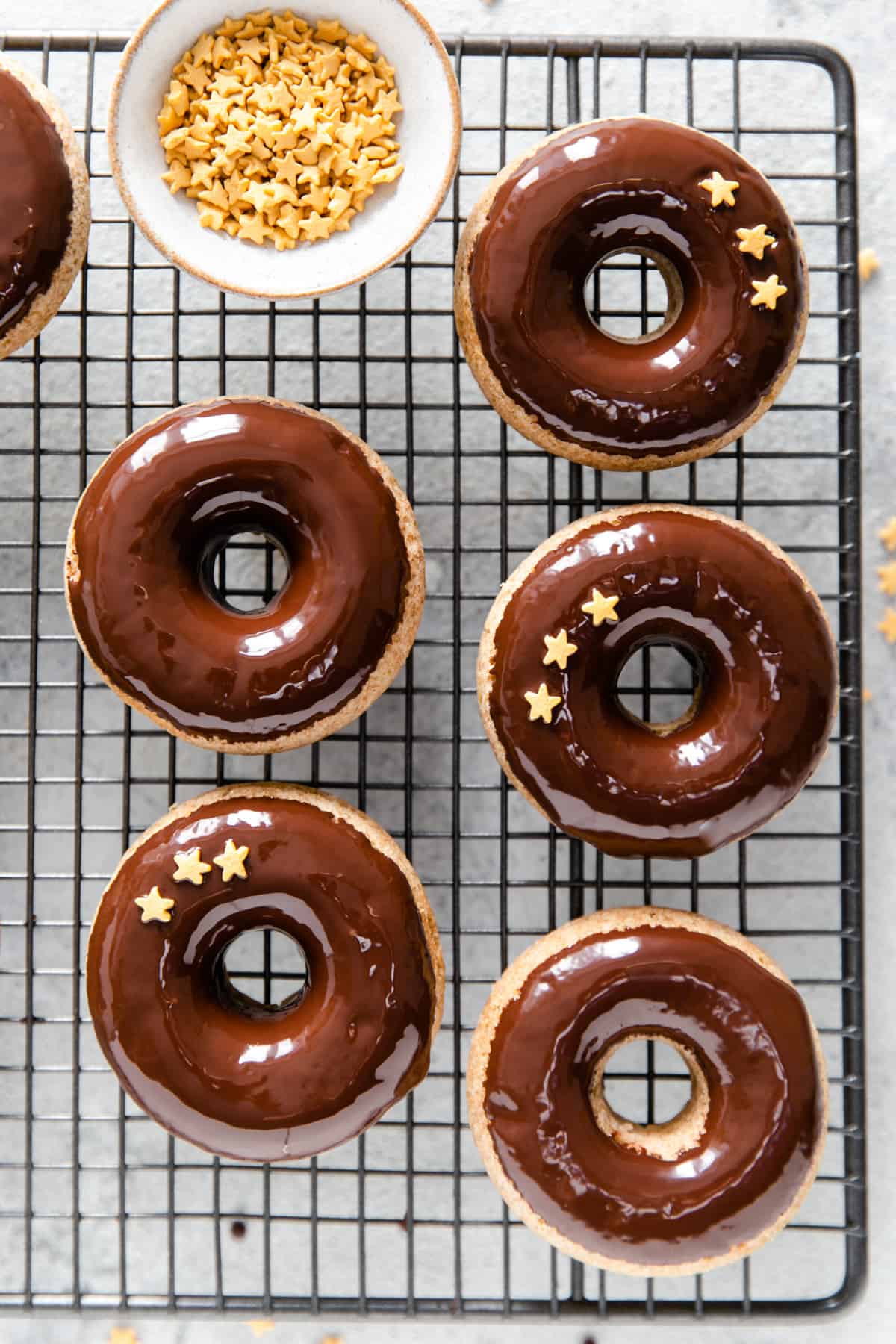 overhead shot of baked doughnuts dipped in chocolate glaze decorated with small star-shaped sprinkles