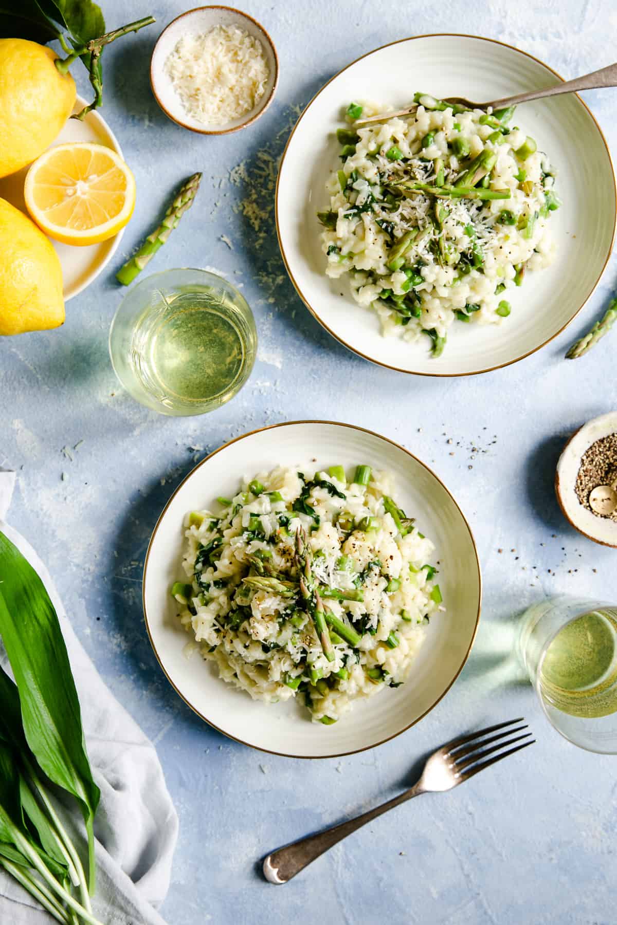 overhead shot of two bowls with wild garlic and asparagus risotto with a glass of white wine on side